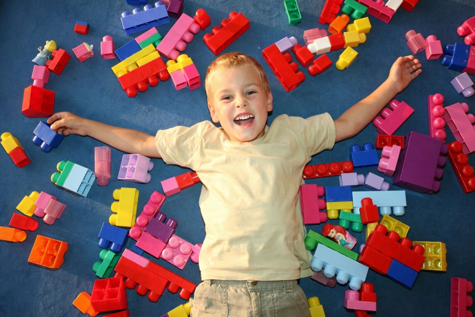 Happy child lying on colorful building blocks with arms outstretched.