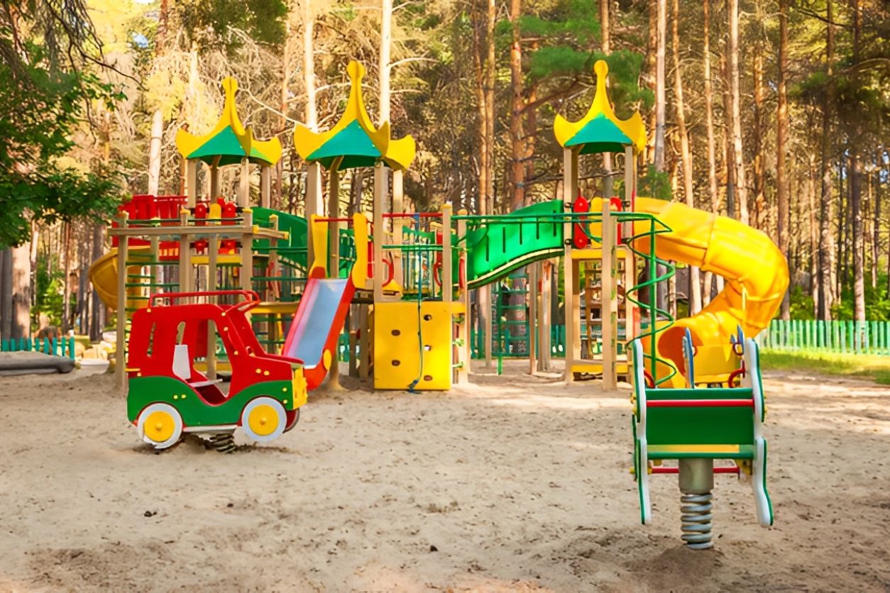 Colorful playground equipment in a forest setting with slides and climbing structures.