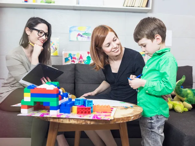 Two women and a boy playing with colorful building blocks at a table.