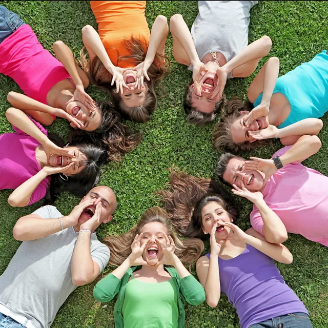 A circle of happy young women lying on grass, making peace signs.