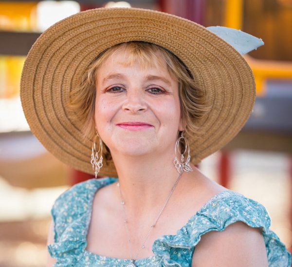 Smiling woman wearing a wide-brimmed straw hat and a blue floral top.