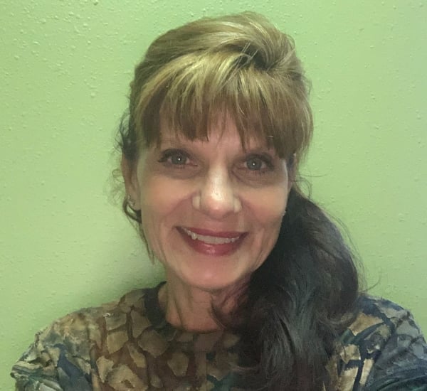 Smiling woman with dark hair against a light green wall.