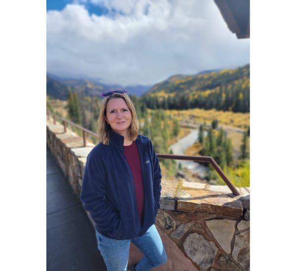 Young woman smiling outdoors with scenic mountains in the background.