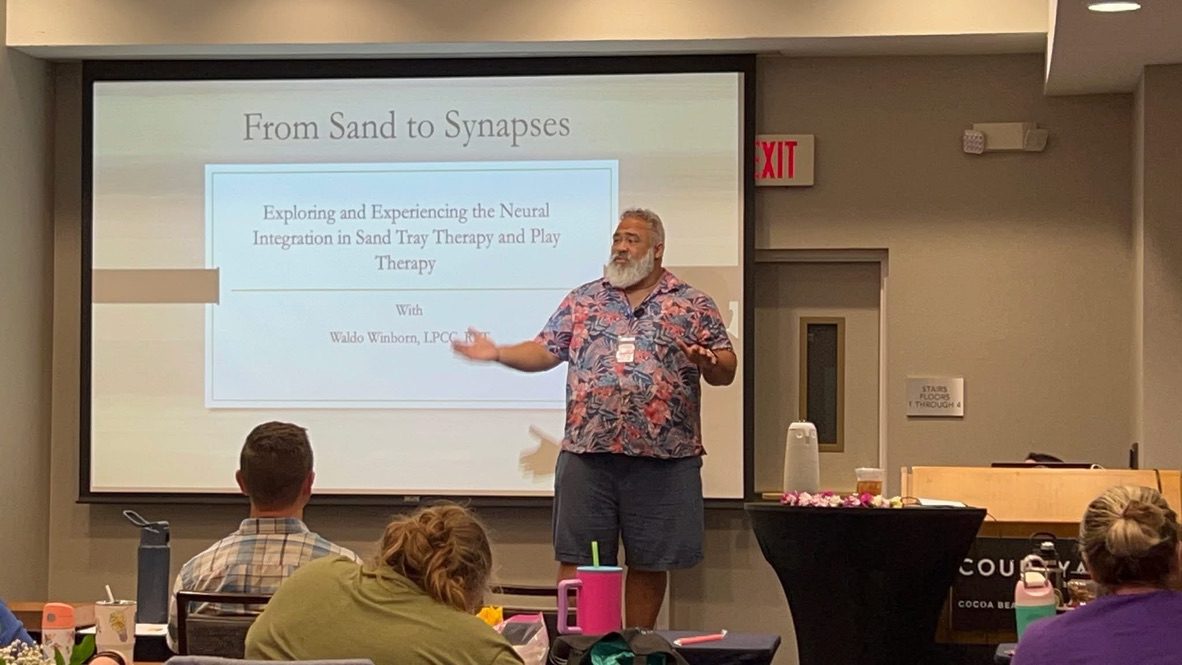 A man presenting in front of an audience in a conference room.