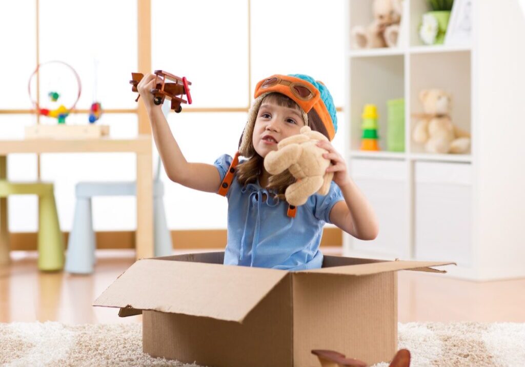 Little girl playing with toys inside a cardboard box.