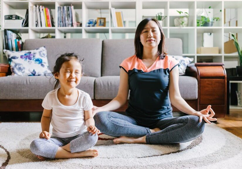 Mother and daughter meditating together on the floor at home.