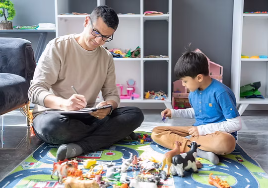 A father and son playing and drawing together on the floor surrounded by toys.